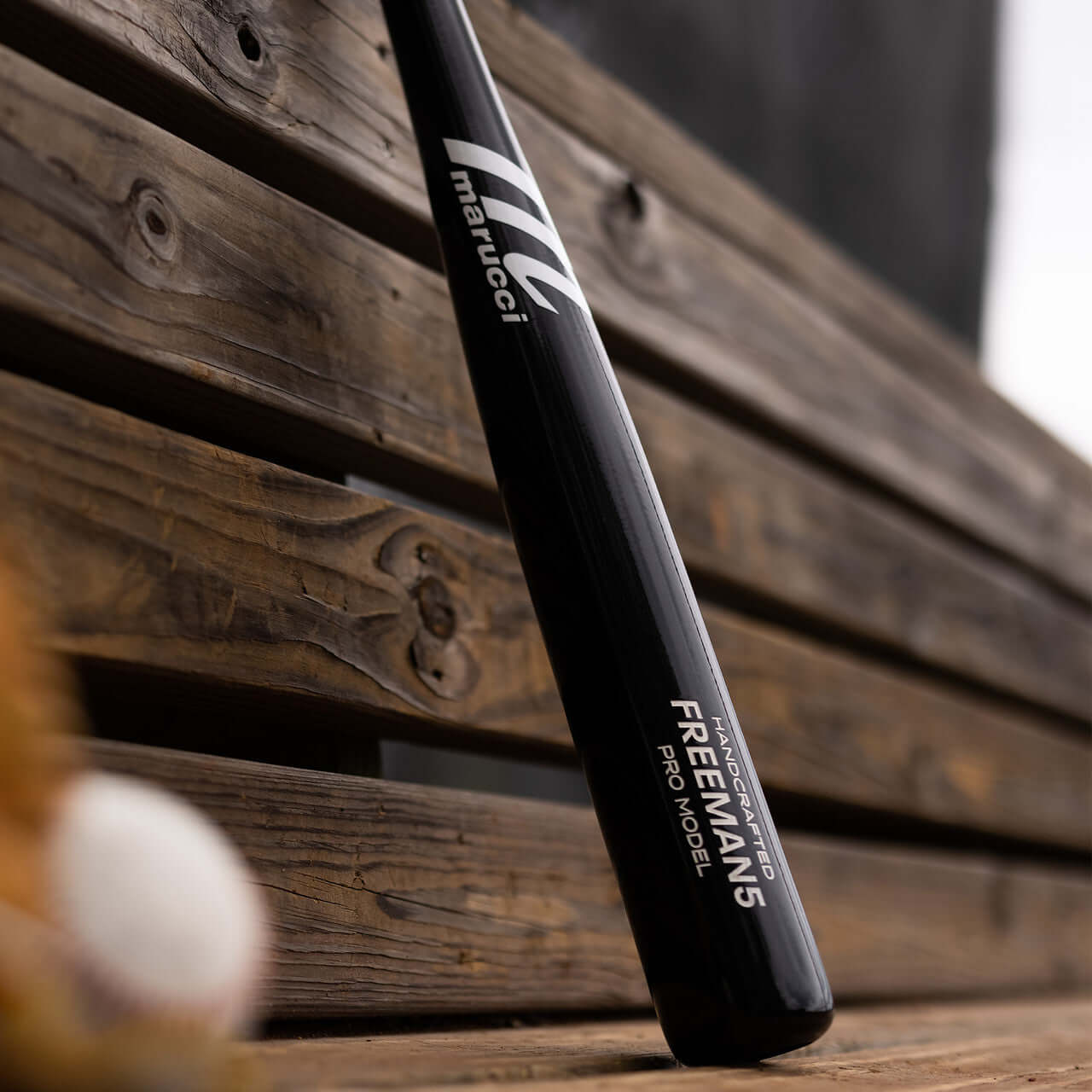 Marucci Freeman5 Pro Model Black bat resting on a wooden bench, showcasing its traditional knob and end-loaded design.
