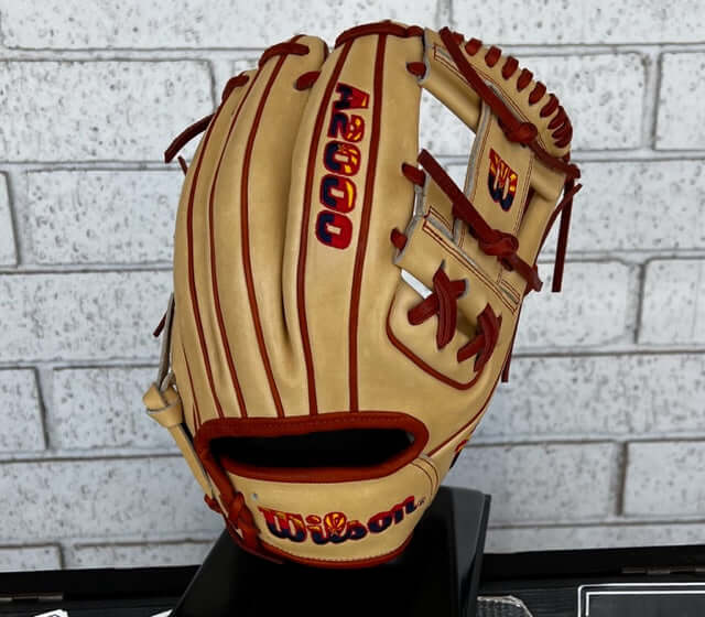 Wilson A2000 AZ Flag Logo 1786 baseball glove in blonde leather with red accents against a brick background.