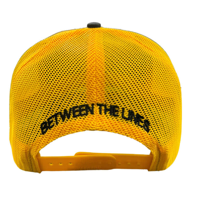 Back view of Richardson BTL 112 Split Black/Gold cap, showing yellow mesh and "Between The Lines" text above the adjustable strap.