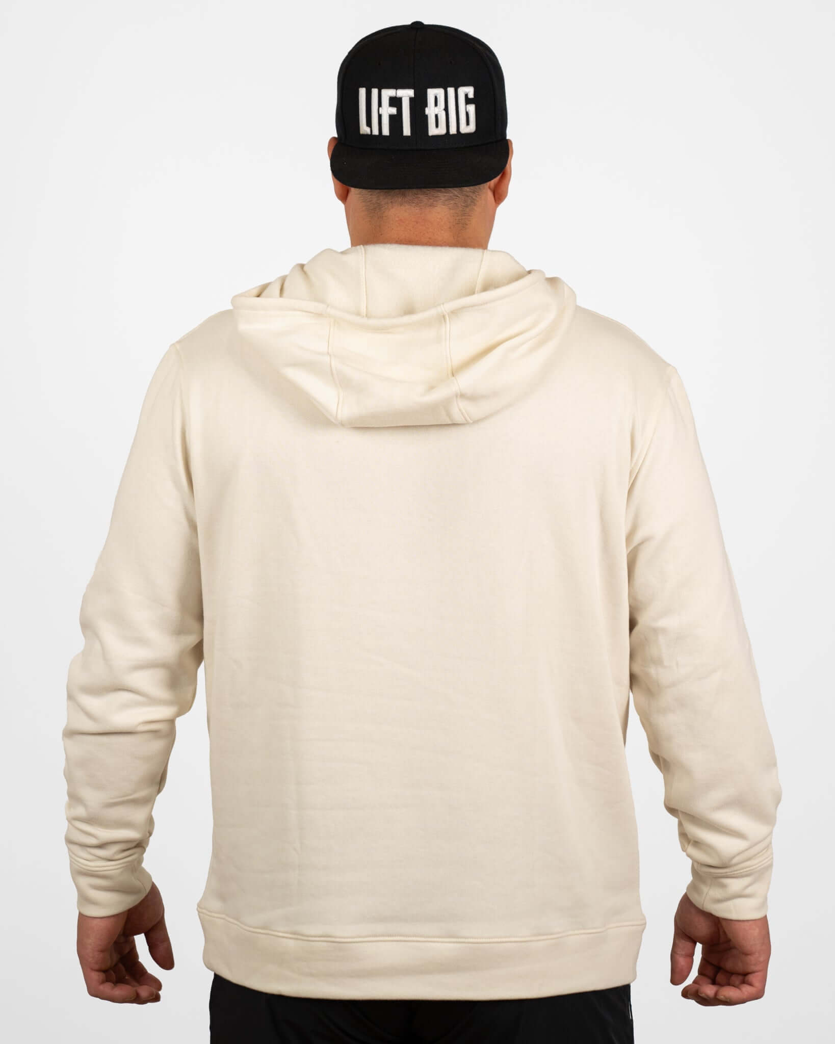 Back view of a man wearing a tan heavyweight hoodie, ideal for athletic recovery and comfort, with a 'Lift Big' cap.