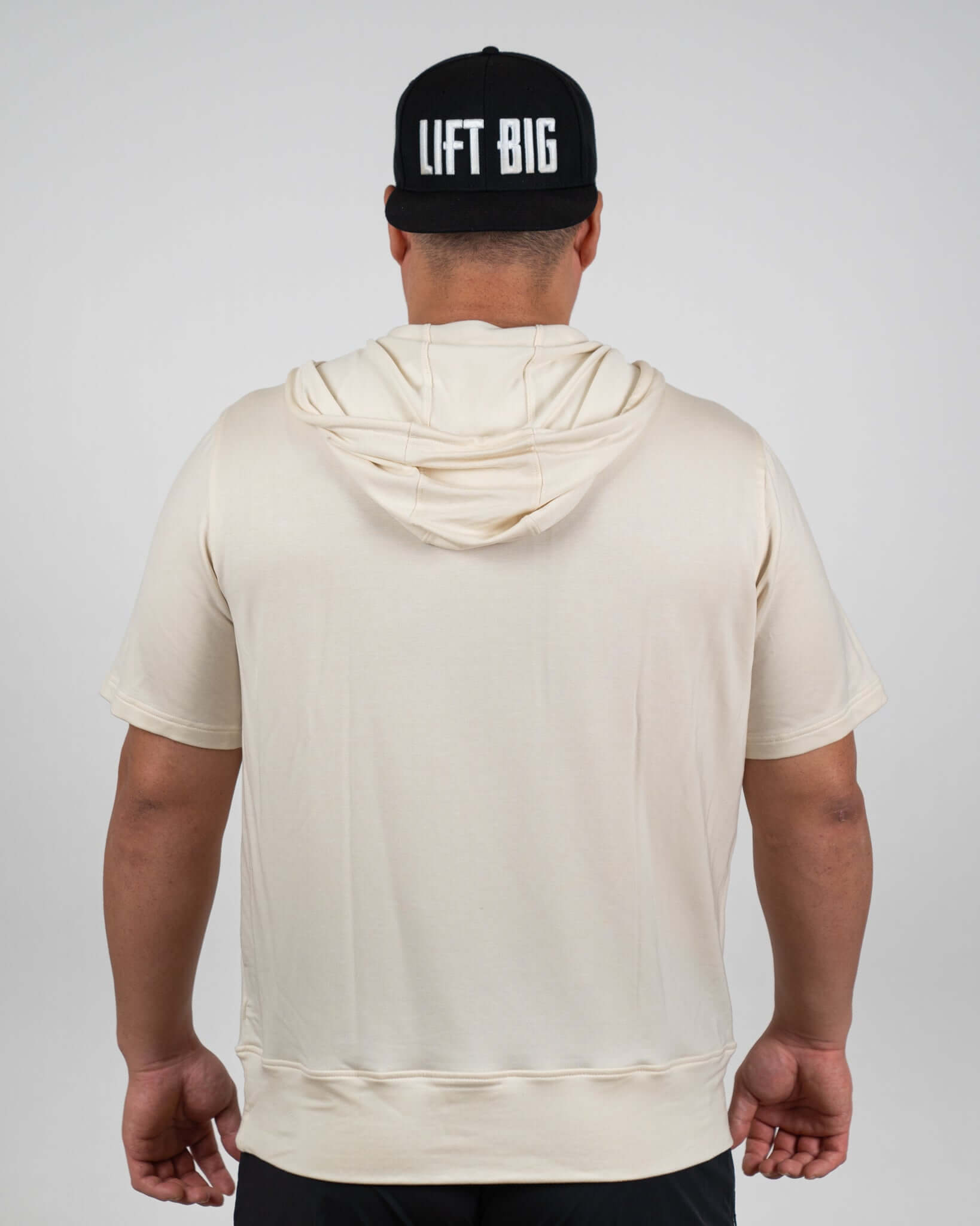 Rear view of a man wearing the King of Juco Tan Short Sleeve Hoodie with a black 'Lift Big' cap.
