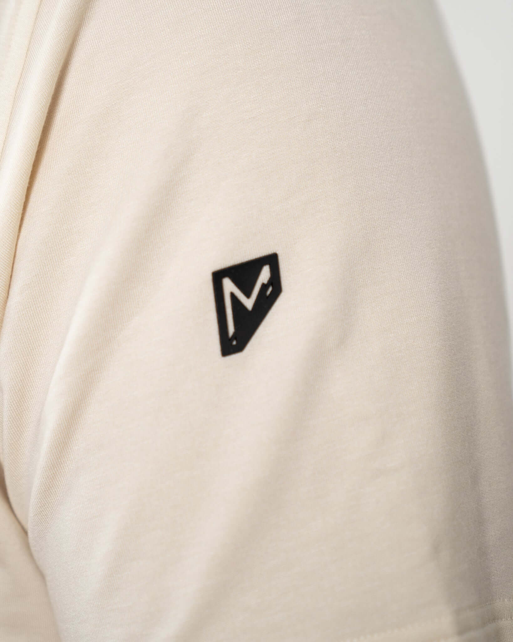 Close-up of the black logo on the sleeve of the King of Juco tan short sleeve hoodie.