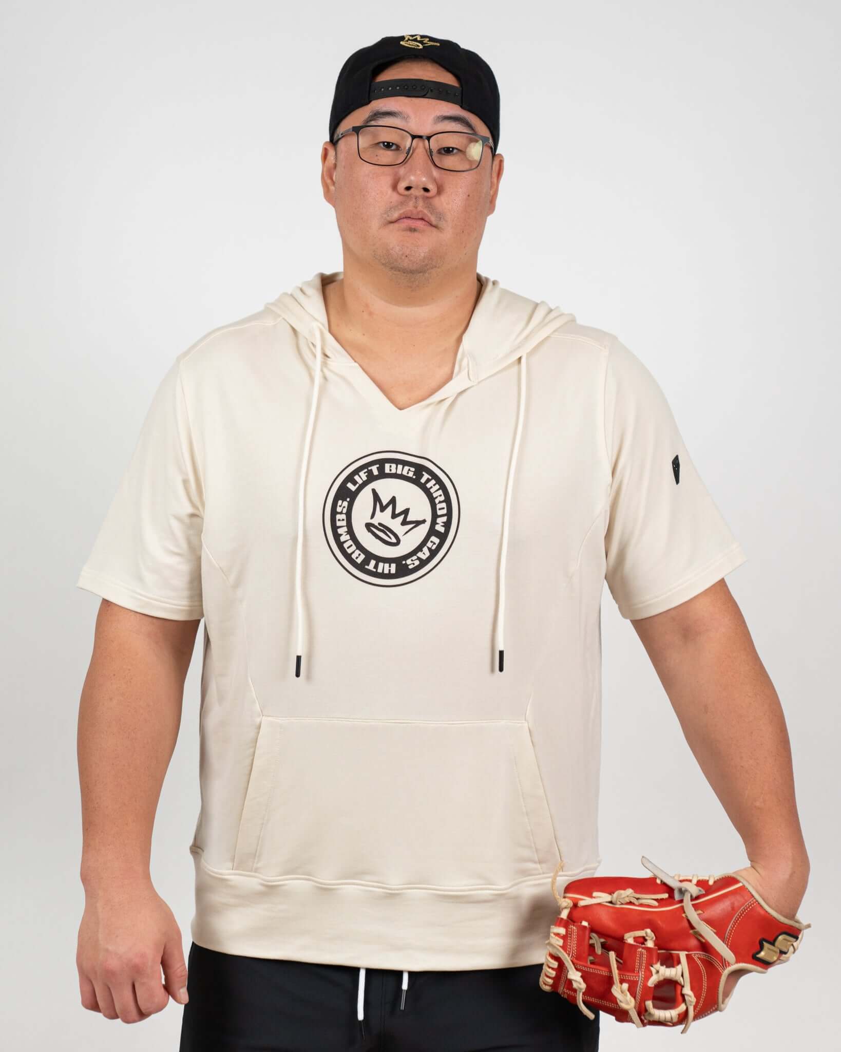 Model wearing the King of Juco Tan Short Sleeve Hoodie with a notch-neck collar, holding a baseball glove.