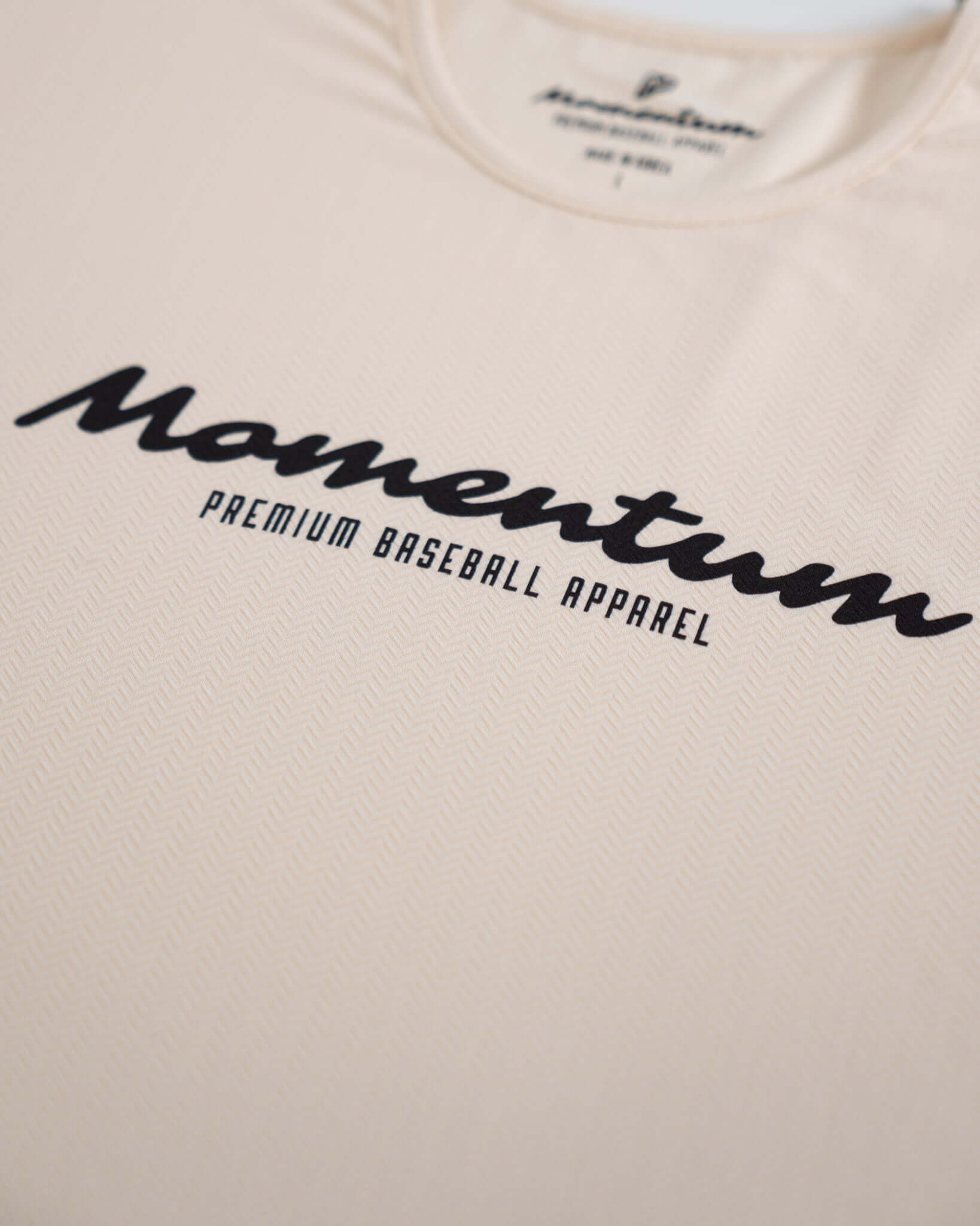 Close-up of Momentum Tan Recovery Tee featuring Premium Baseball Apparel logo on soft fabric.