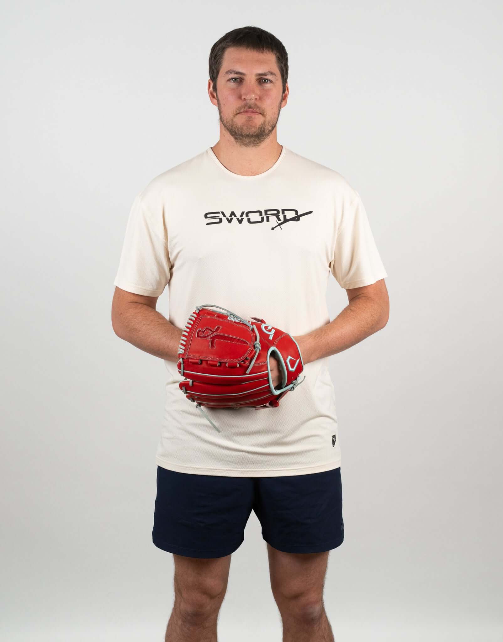 Man wearing a beige SWORD tee and holding a red baseball glove, ready for a game.