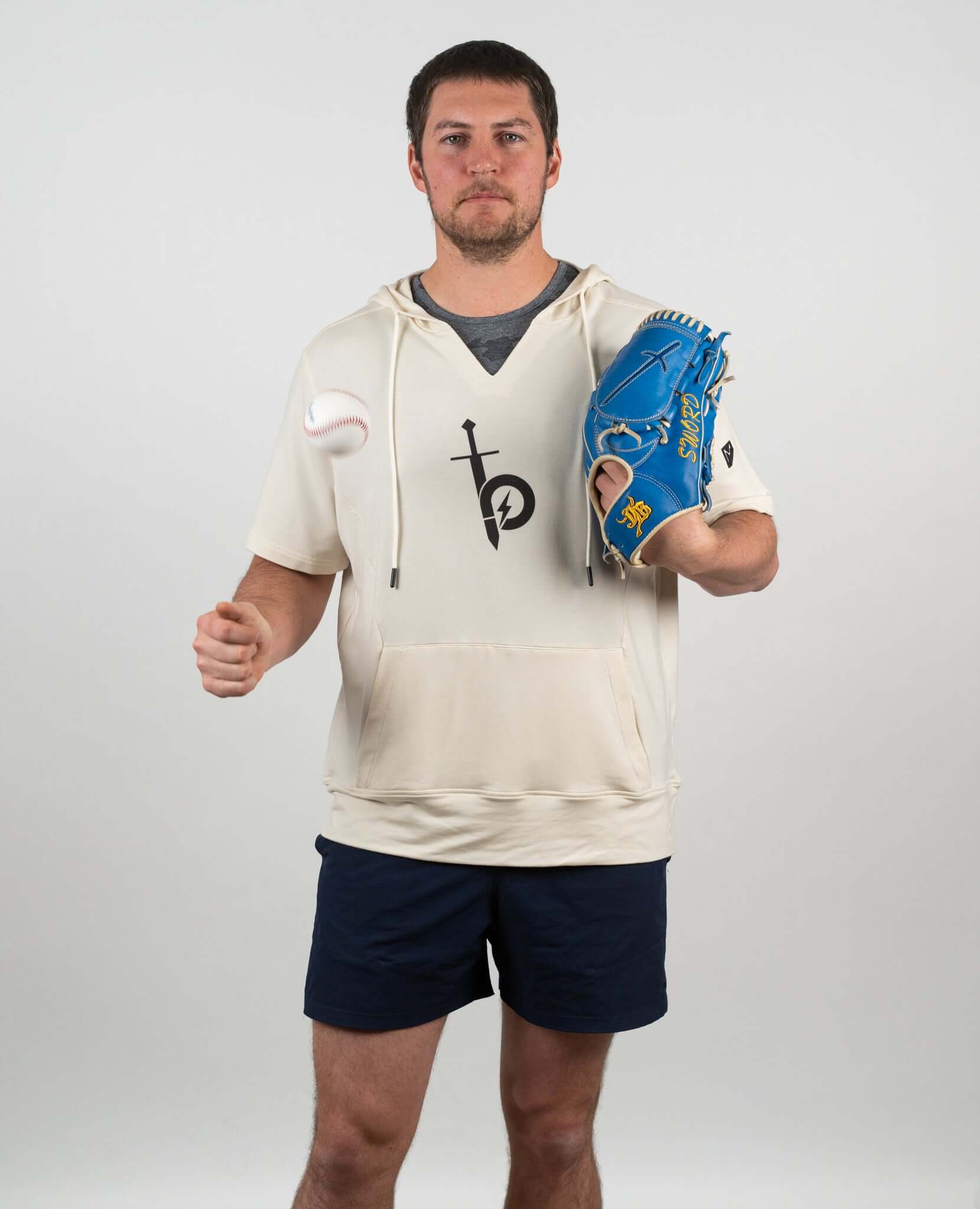 Man wearing Bauer OutageTan Short Sleeve Hoodie, holding a baseball and glove, ready for training or casual wear.