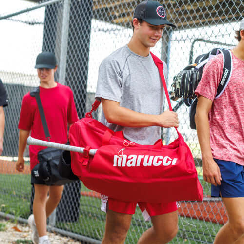 Young athlete carrying a Marucci Team Utility Duffel Bag V3 with bats on a baseball field.