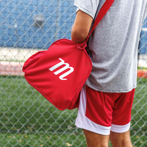 Marucci Team Utility Duffel Bag V3 in red carried by an athlete in sports attire near a fence.