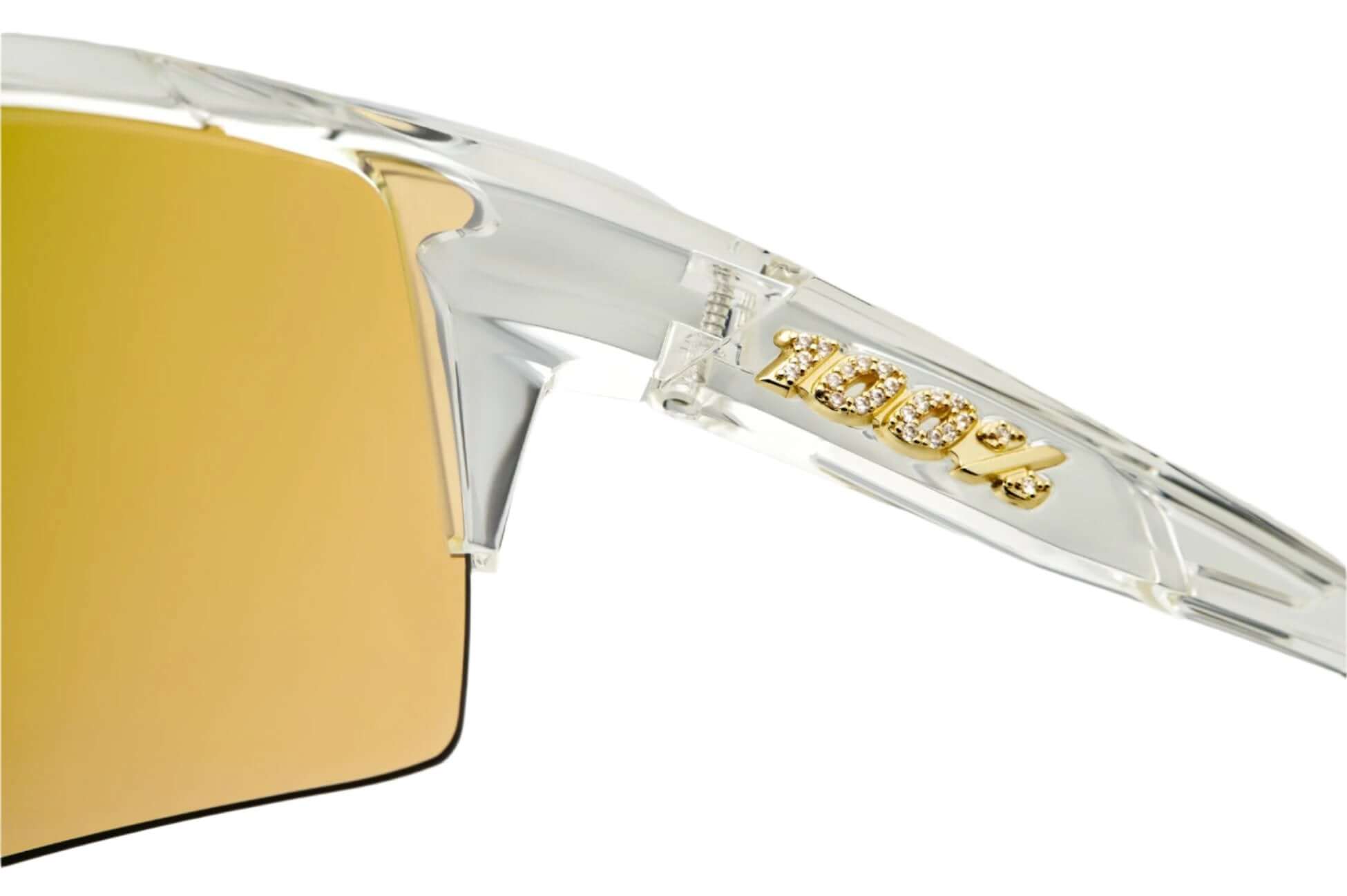 Close-up of 100% Speedcraft sunglasses showcasing gold HiPER lens and iced-out logo detail.