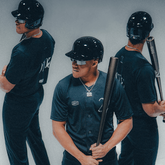 Baseball player posing in black uniform and helmet, holding a bat, showcasing athletic gear and confidence.