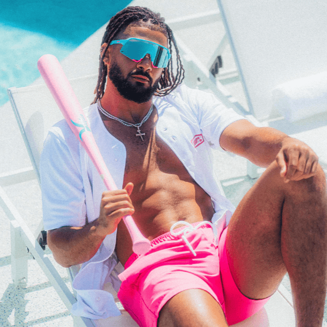 Man in blue sunglasses and pink shorts lounging by pool with baseball bat, showcasing sporty style and sunglasses.