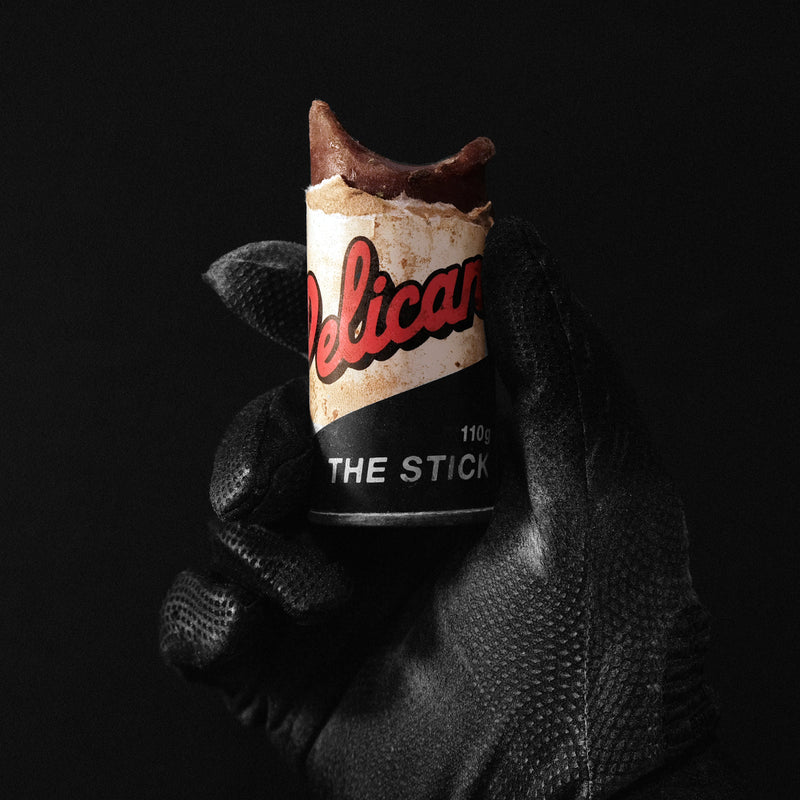 Hand holding a cylindrical product labeled 'The Stick' with 'Delicat' branding against a black background.