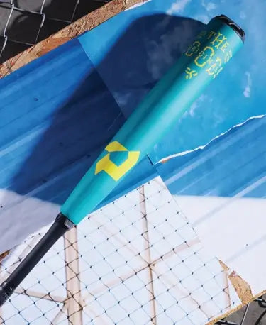 DeMarini The Goods Teal BBCOR 2025 bat featured on a textured background with blue and white elements.