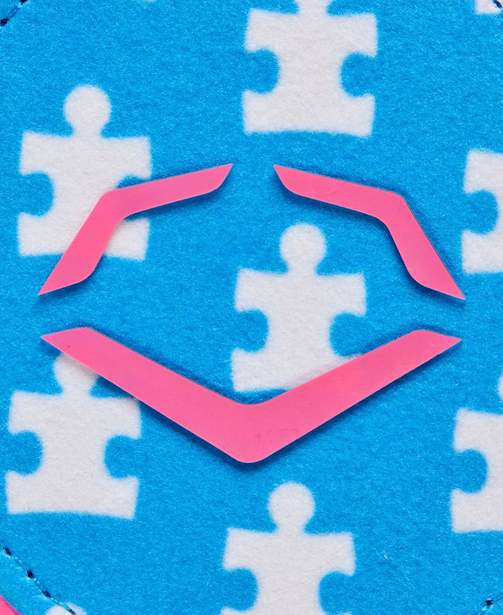 Close-up of blue fabric with white puzzle pieces and pink EvoShield logo, symbolizing inclusion and support.