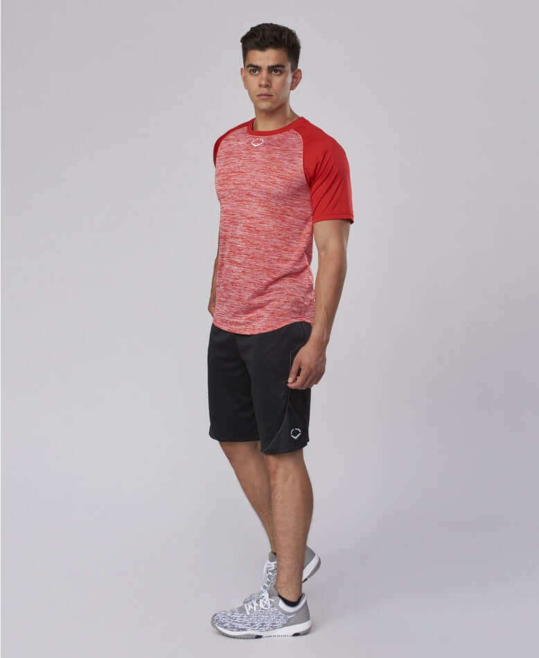 Man wearing Evoshield Adult E304 Performance Pullover Tech Tee in scarlet, paired with black shorts and athletic shoes.