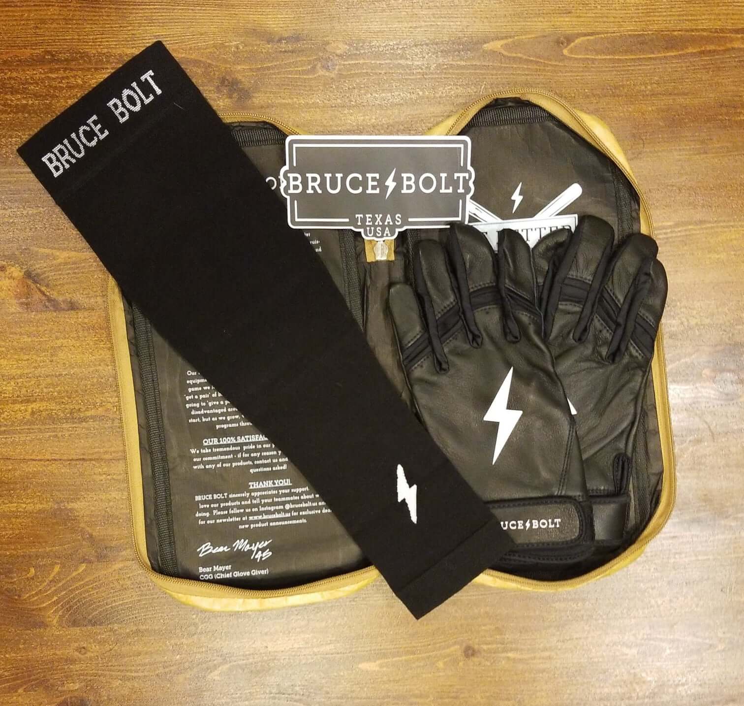 Bruce Bolt black arm sleeve and gloves displayed in a wooden tray with branding.