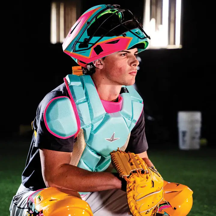 Catcher wearing All-Star MVP-Pro Short Fuse Kit with helmet, chest protector, and shin guards in Yellow/Pink/Seafoam, side view.
