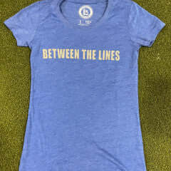 Between The Lines women's t-shirt in blue with stylish text graphics on a green background.