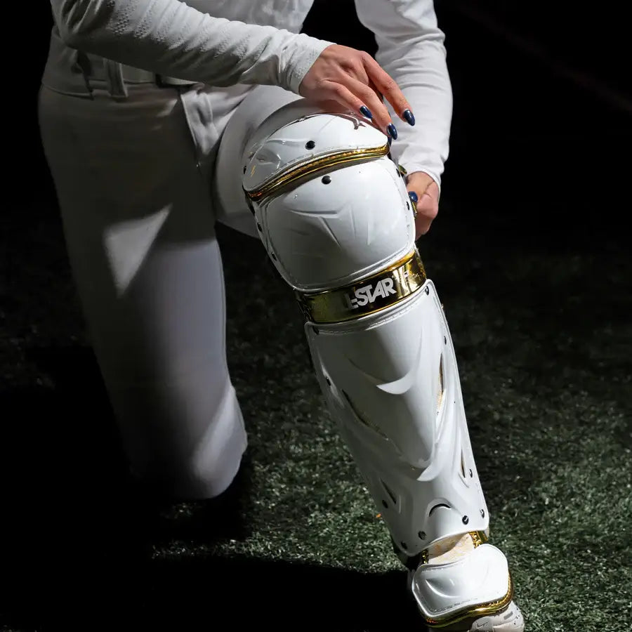 All-Star MVP Pro PHX™ Diamond Series Catcher's Kit leg guard in White/Gold being adjusted, highlighting knee protection.