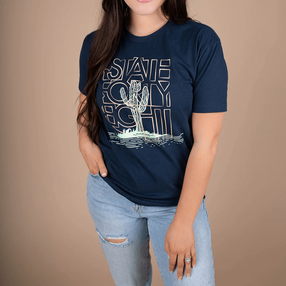 Woman wearing State Forty Eight Men's Crew Neck Saguaro Party Navy shirt with vibrant cactus graphic on a neutral background.