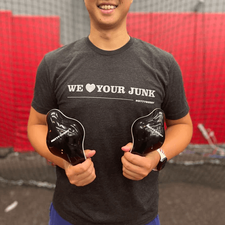 Man wearing NuttyBuddy "We ❤ Your Junk" athletic fit shirt in Vintage Black, holding two black products in a gym setting.