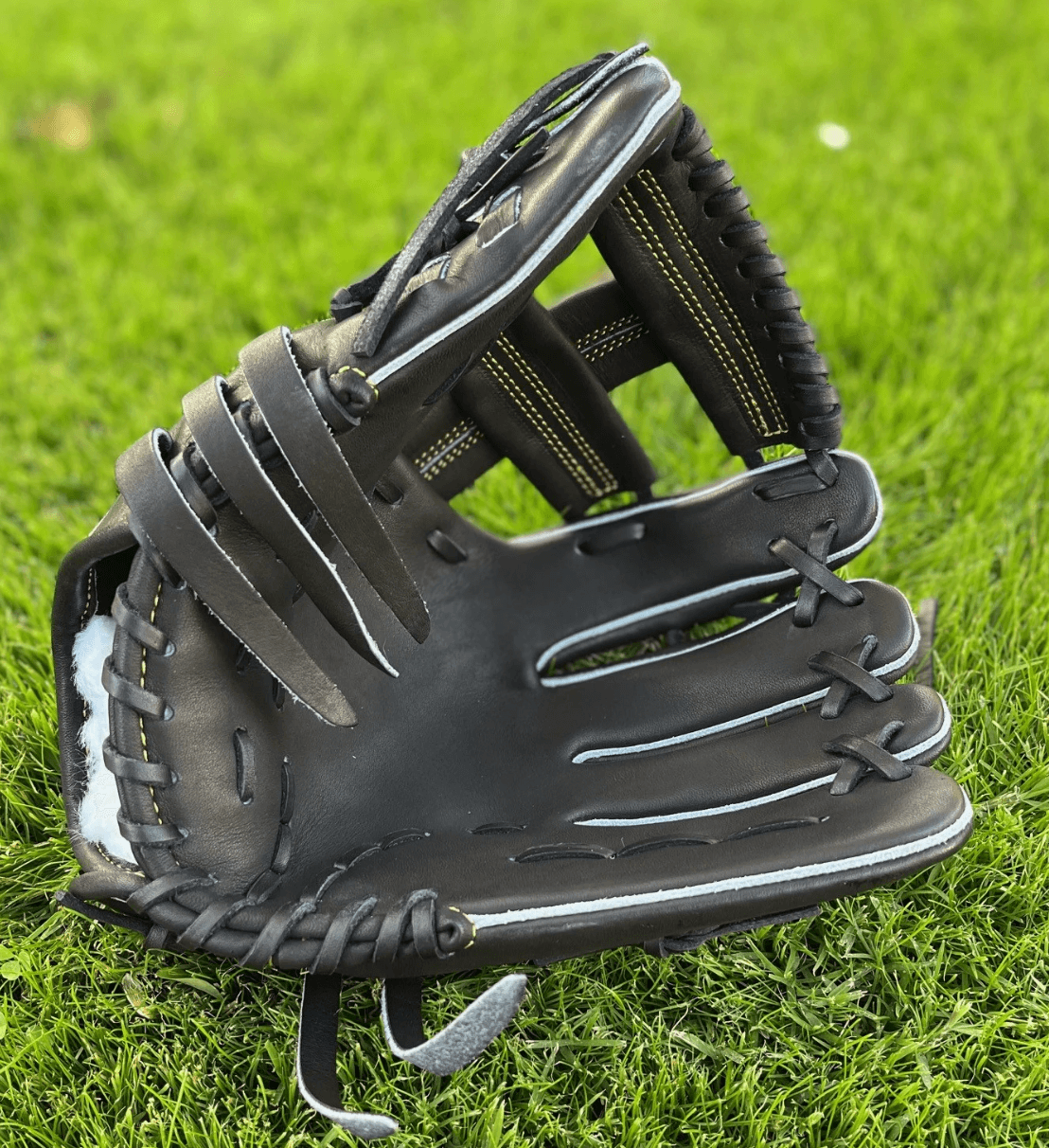 Close-up of The Glove Lab 11.5 INF infielders glove, black steerhide leather on green grass background.
