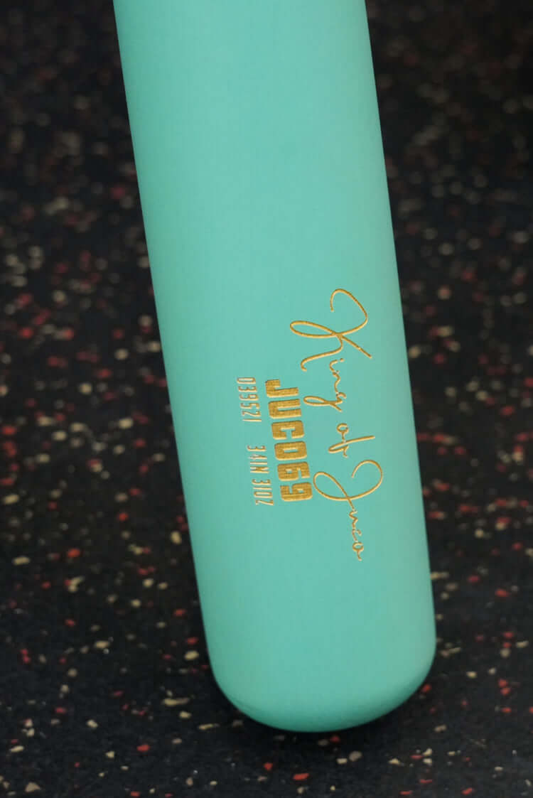 Close-up of the King Of Juco V.2 Matte Mint Wood Bat handle with gold logo engraving on a dark speckled background.