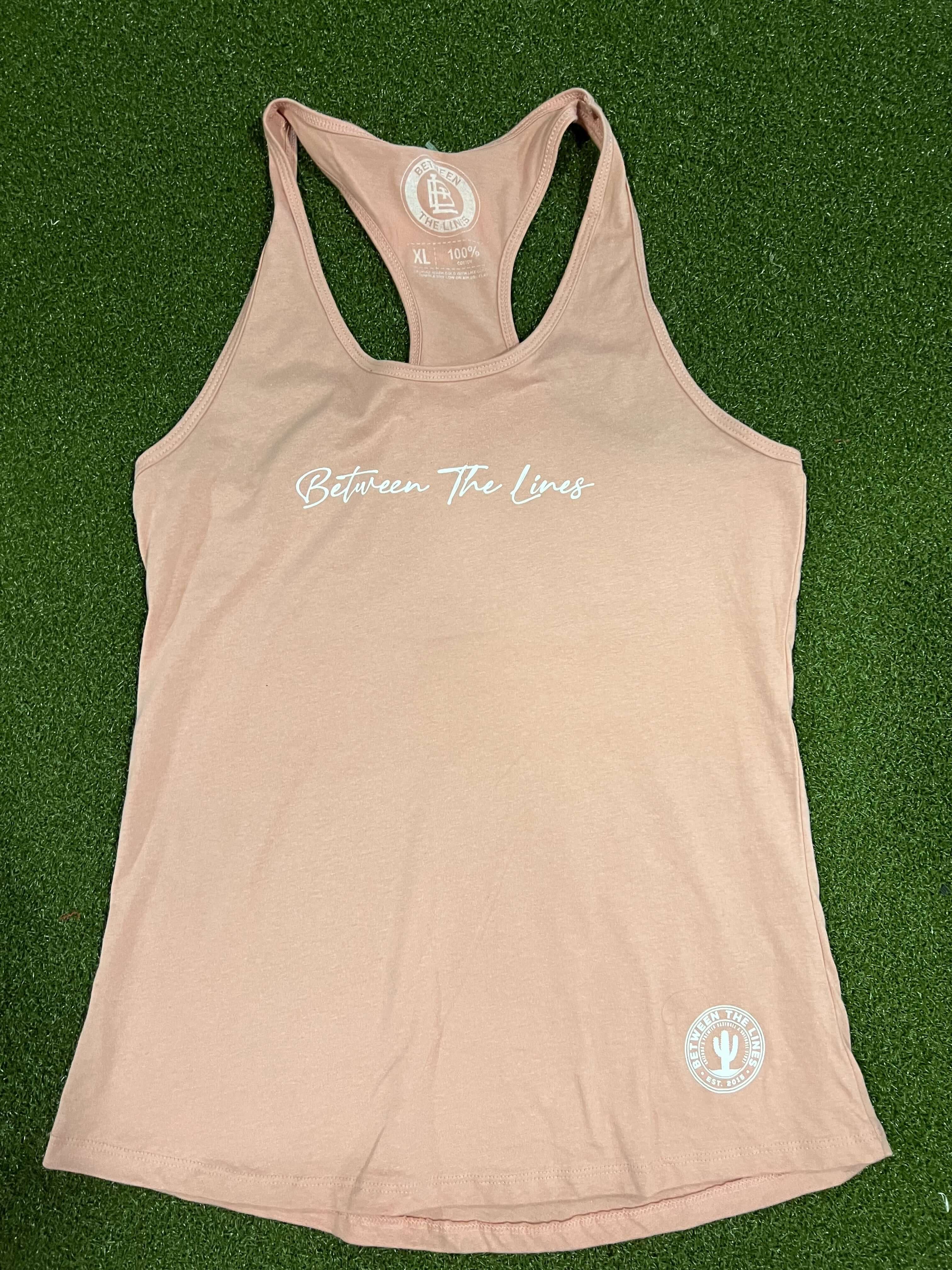 Between The Lines Racerback Women's T-Shirt in light pink on green background, showcasing its trendy sleeveless design.