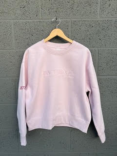 Light pink Baseball Mom Crew sweatshirt hanging on a wooden hanger against a textured gray wall.