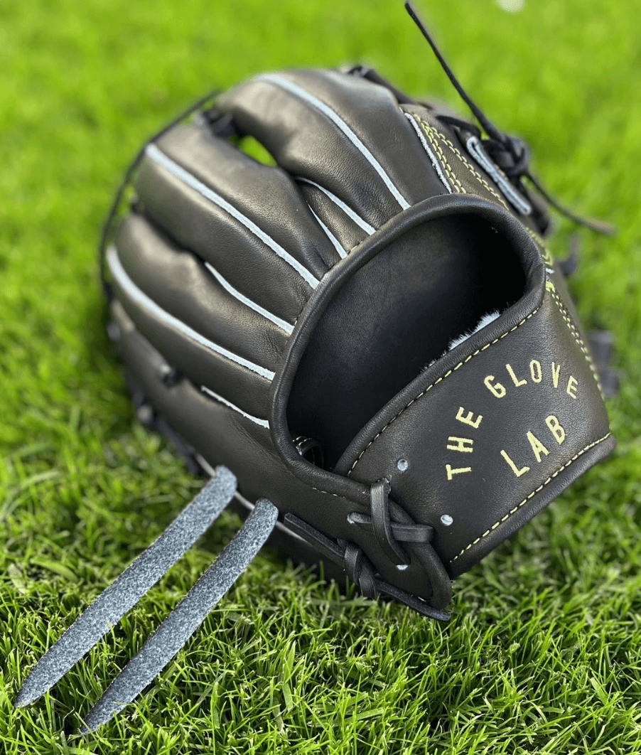 The Glove Lab 11.5 INF single post glove in black leather on green grass, showcasing gold embroidery and laces.