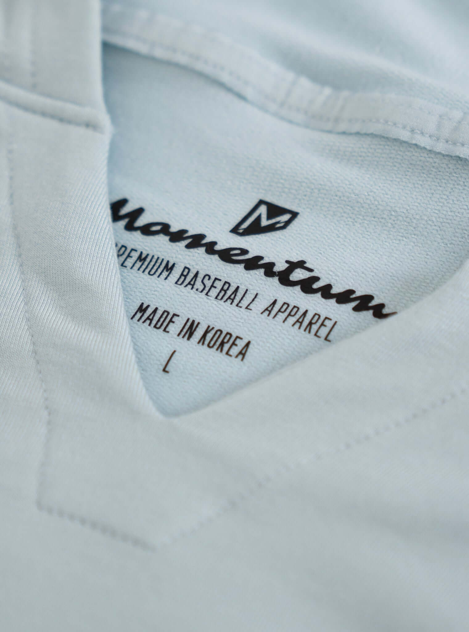 Close-up of the label on a light blue shirt by Momentum, indicating premium baseball apparel made in Korea.
