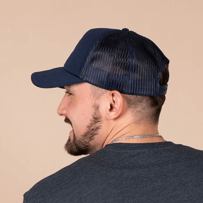 Man wearing a navy foam trucker hat with a mesh back, showcasing the hat's curved peak and stylish design.