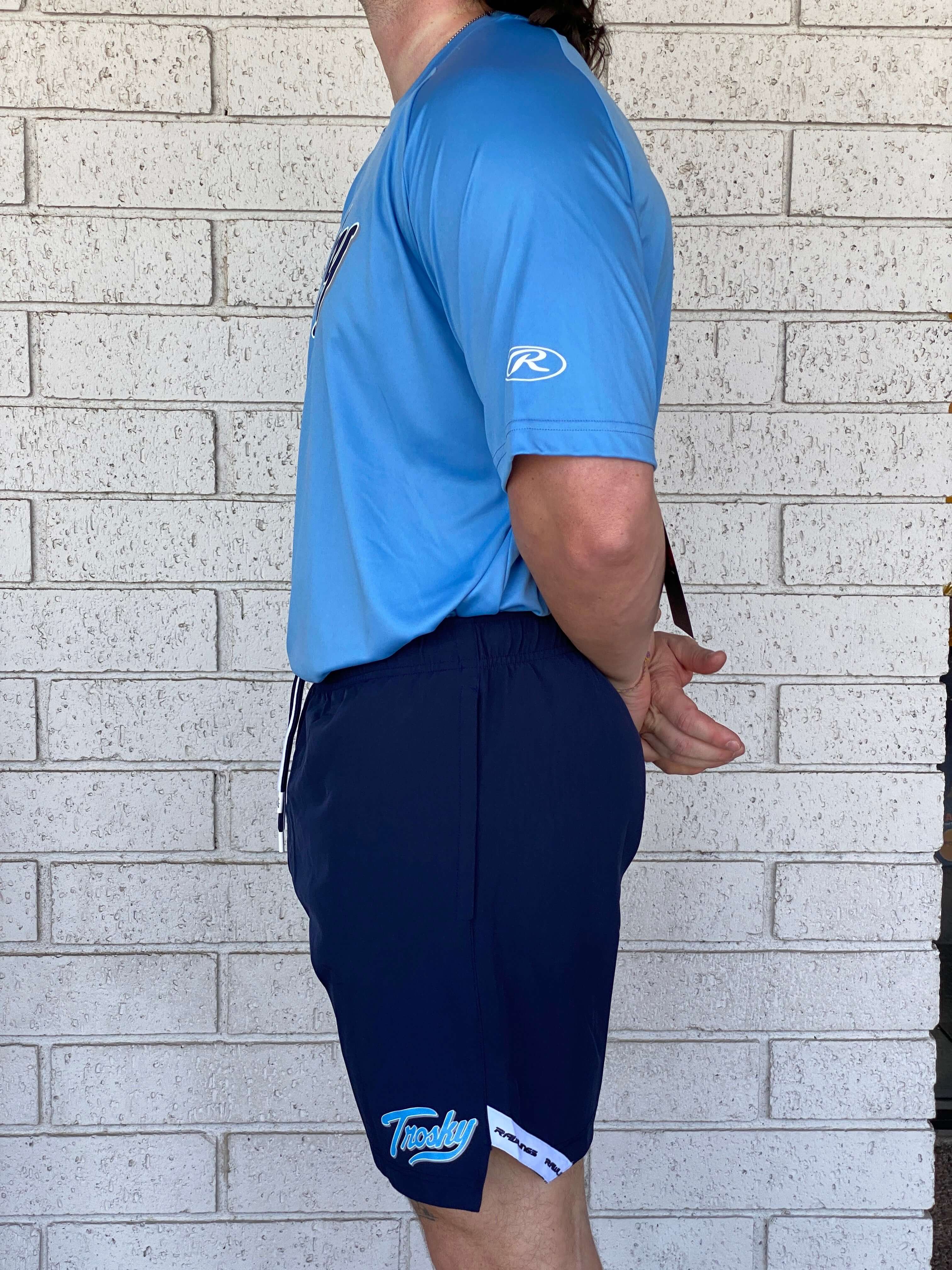 Man wearing Rawlings Trosky Shorts in navy color, showcasing athletic fit and comfort against a brick background.