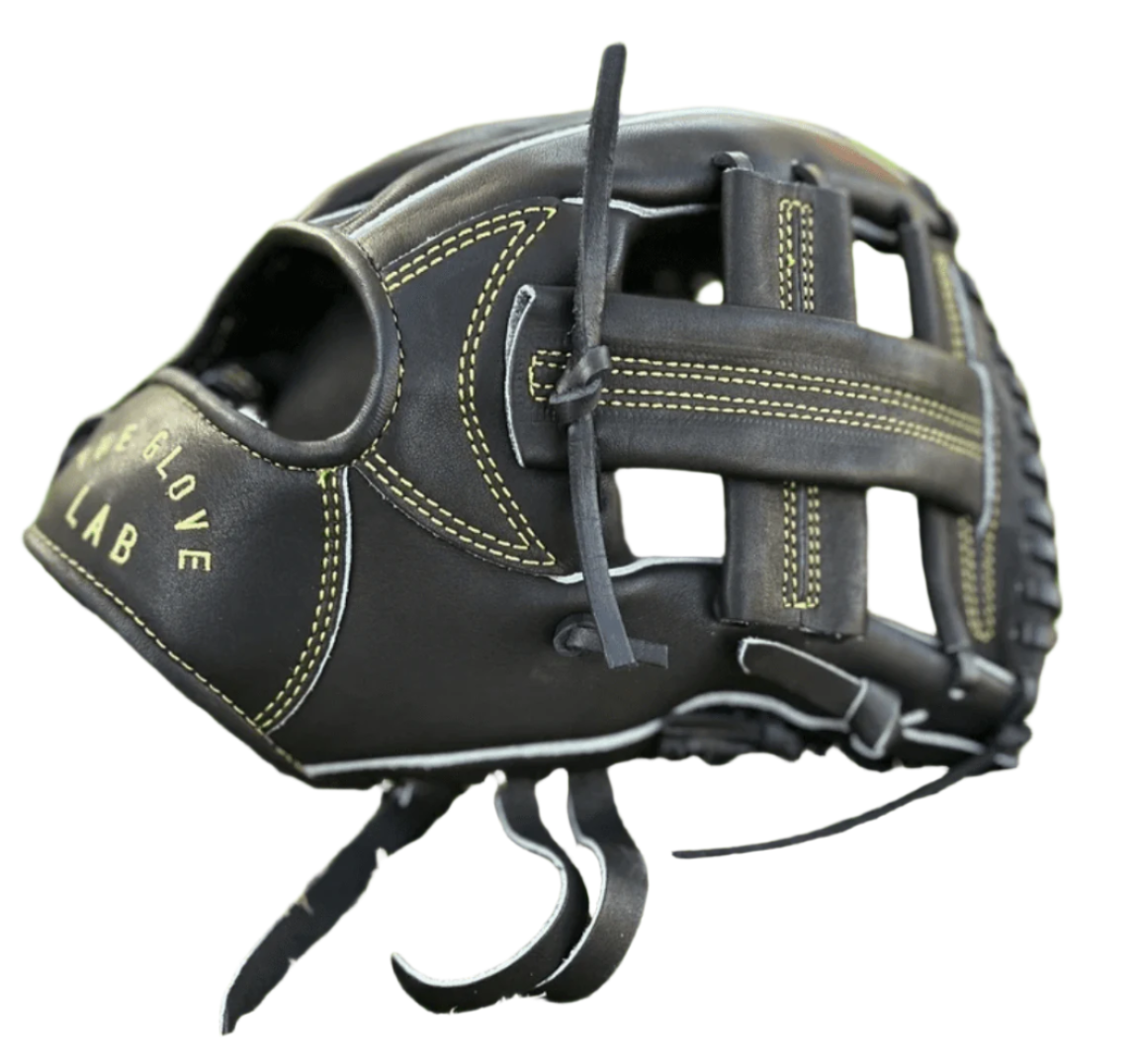 Close-up of The Glove Lab 11.5" INF Single Post glove, showcasing black leather with gold embroidery on green grass.