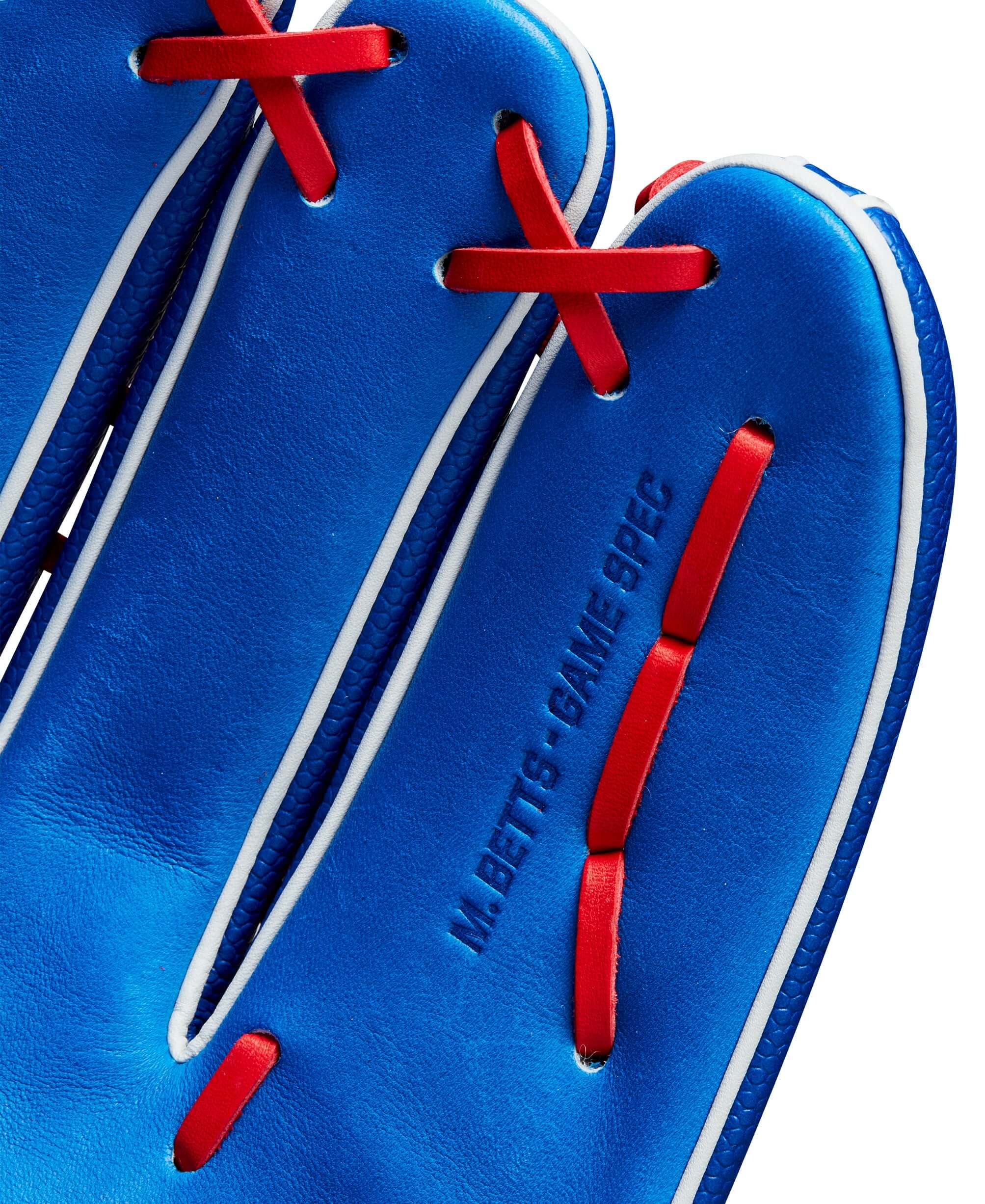 Close-up of the Wilson A2K Mookie Betts game glove, showcasing blue leather with red stitching and "M. Betts Game Spec" detail.