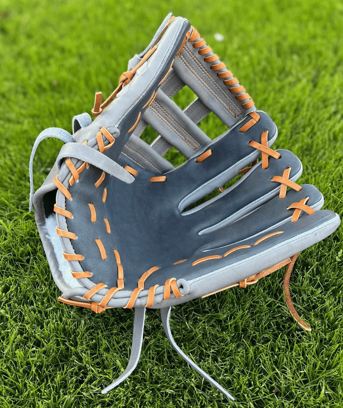 The Glove Lab 12-inch H-Webb glove in grey and navy with tan laces, displayed on green grass.