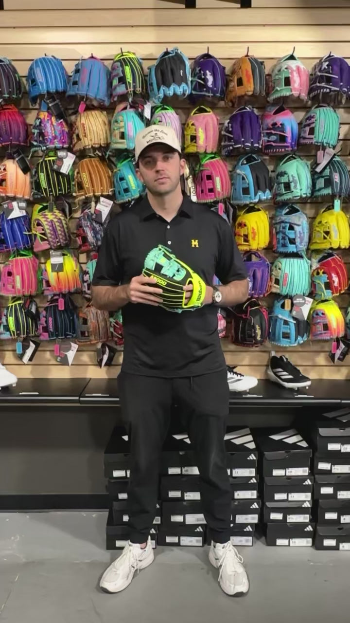 Person holding Wilson 2025 Tennis A2000 1786SS 11.5” Infield Baseball Glove in front of colorful glove display.